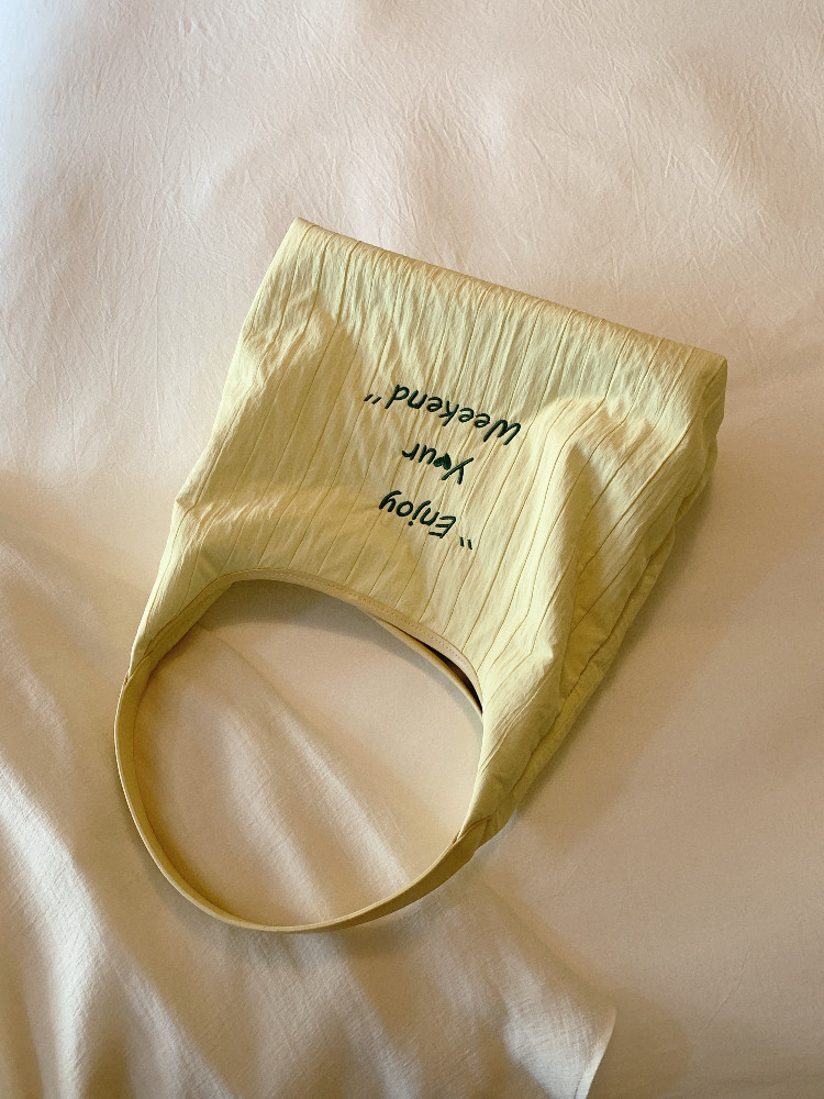 Light yellow tote bag with curved handles and printed text on a fabric background