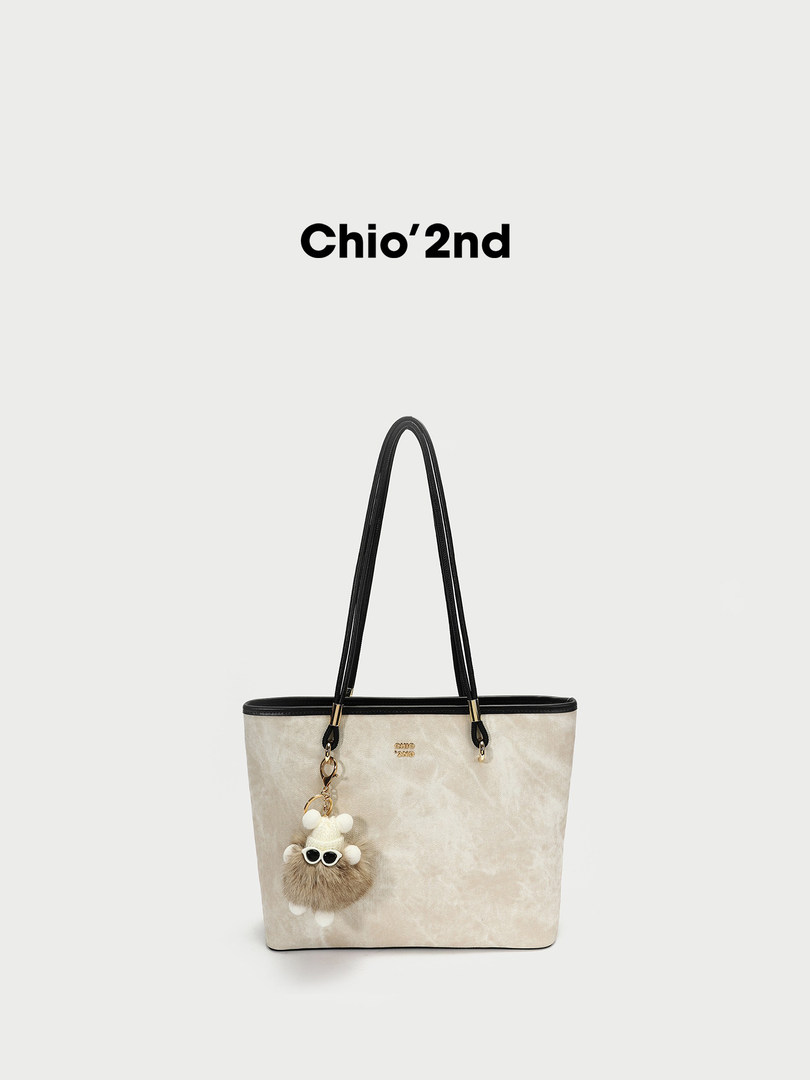 Cream tote bag with black handles and a furry charm on a white background