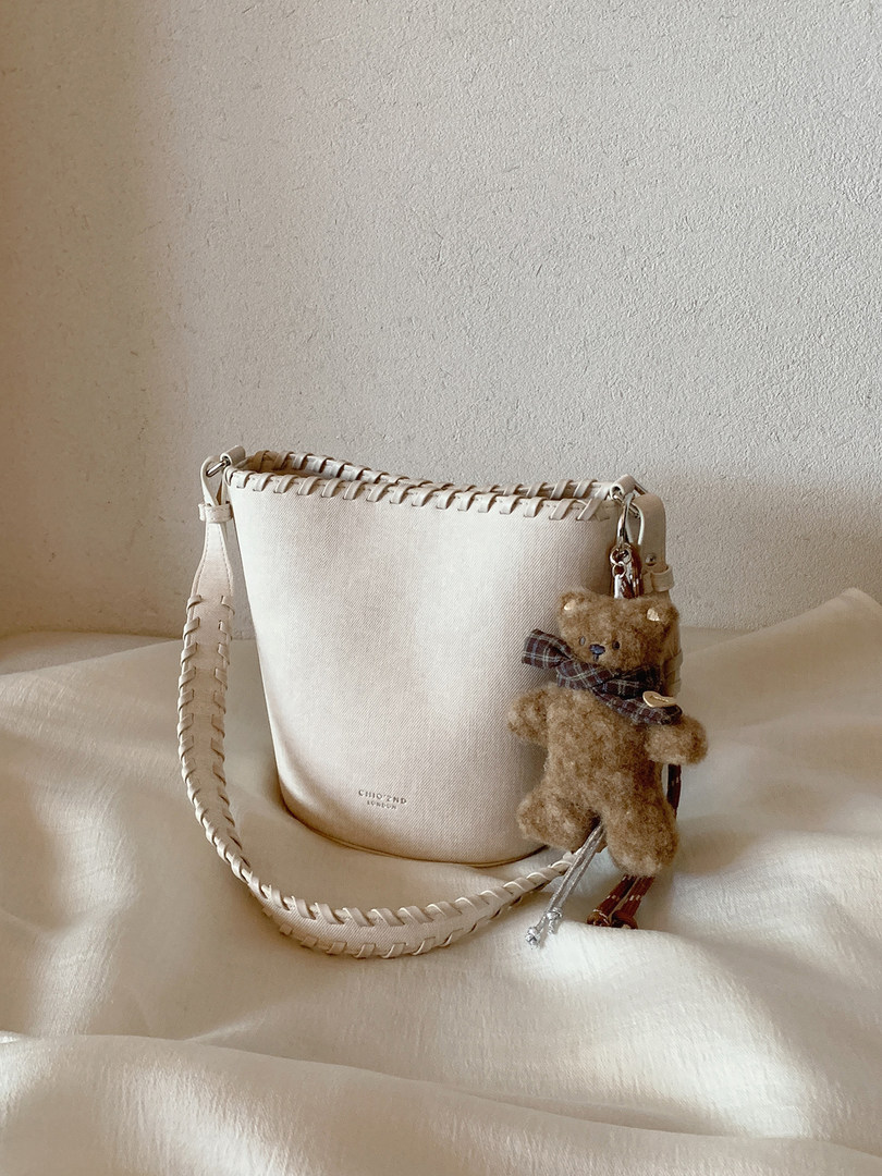 Cream woven shoulder bag with teddy bear charm on a neutral background