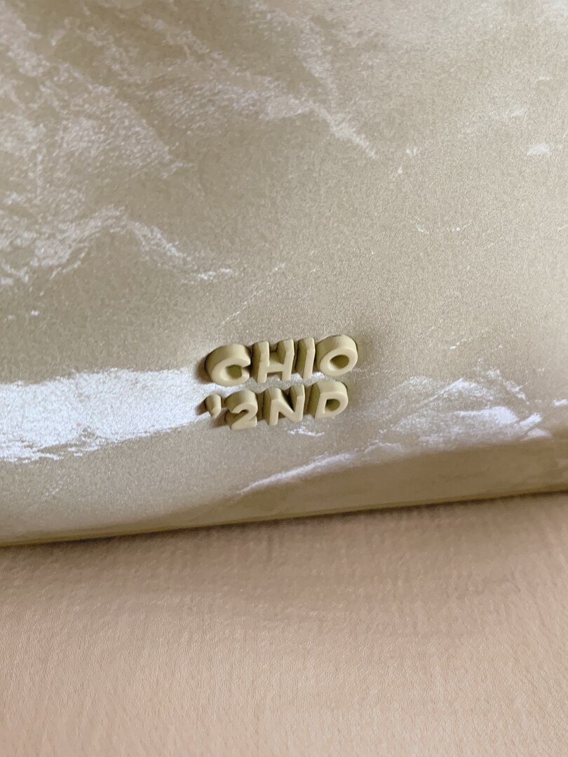 Close-up of a beige textured handbag or pouch with raised logo lettering.