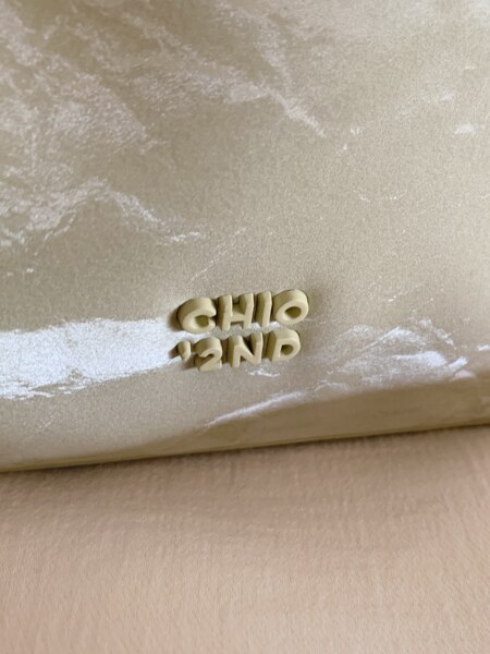 Close-up of a beige textured handbag or pouch with raised logo lettering.