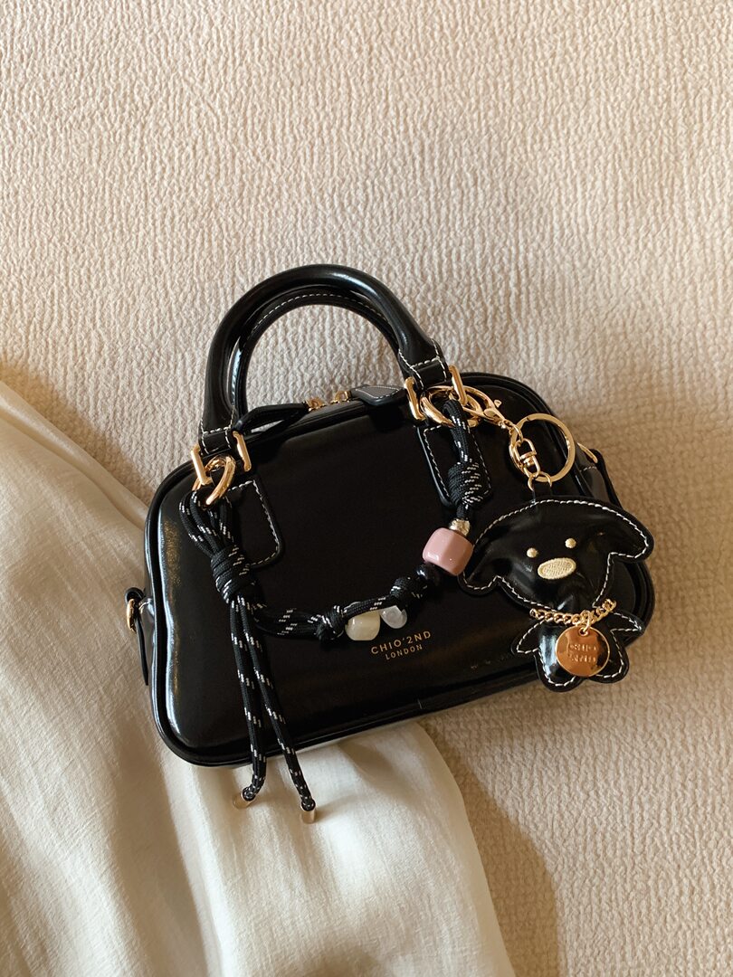 Black patent leather handbag with gold hardware and charm accessories on a neutral background