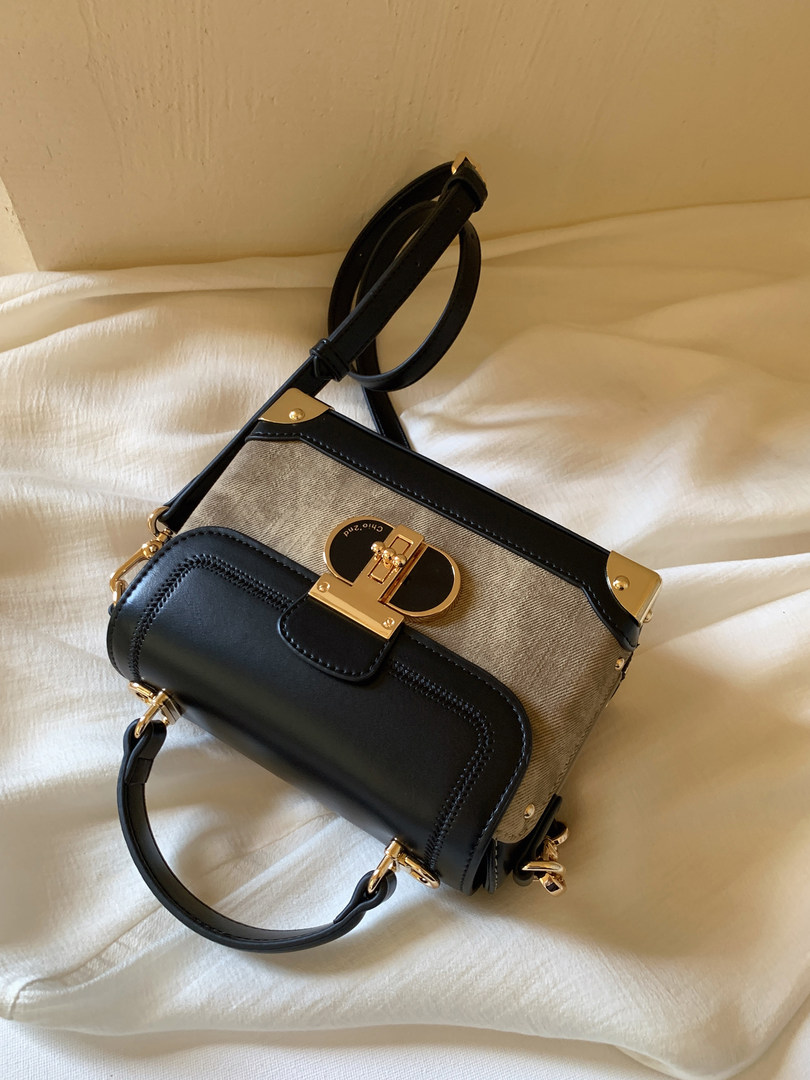 Black and beige designer-style handbag with gold hardware on a bed
