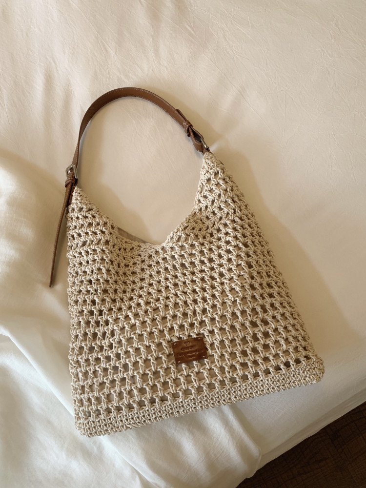 Beige woven shoulder handbag with brown strap on a bed