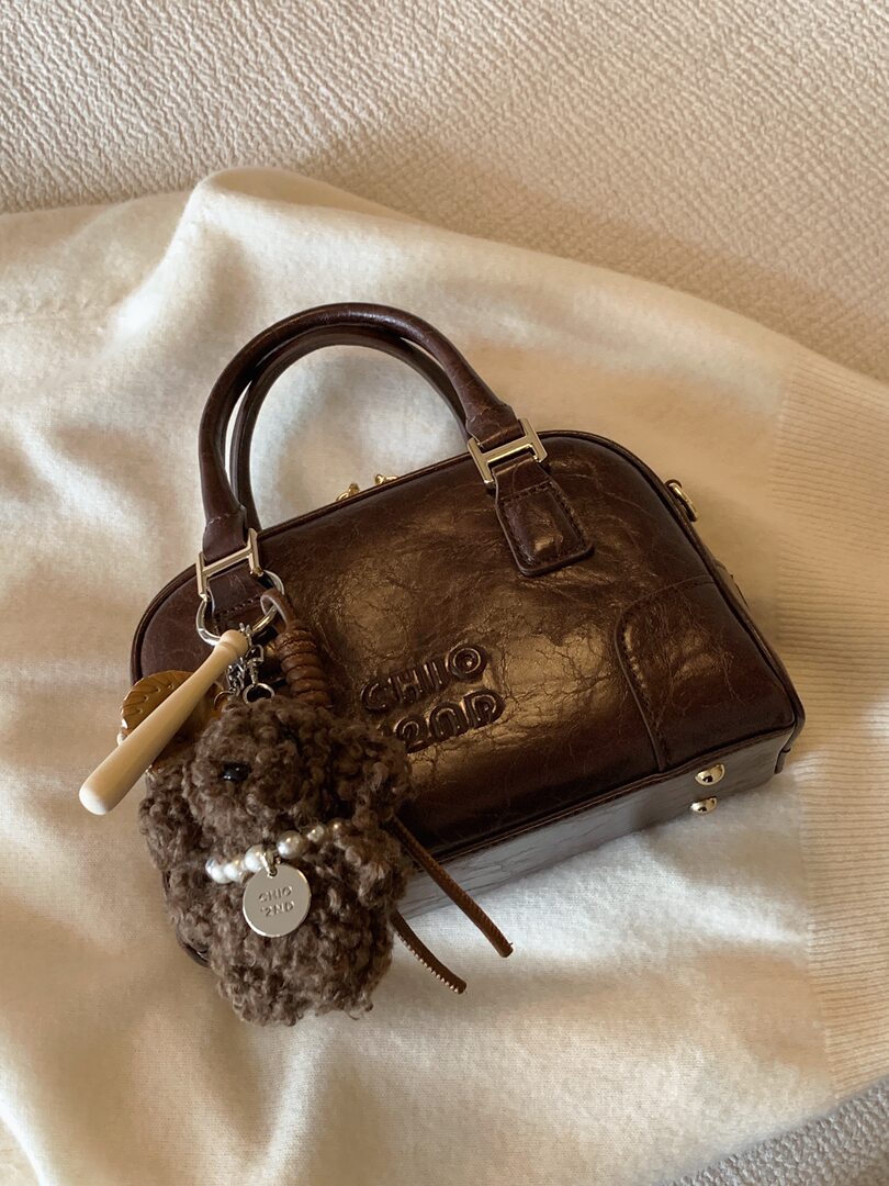 Brown leather handbag with charm on a neutral fabric background