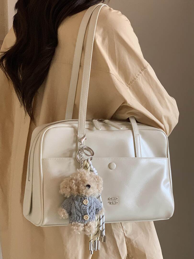 White shoulder handbag worn by a model with a teddy bear charm