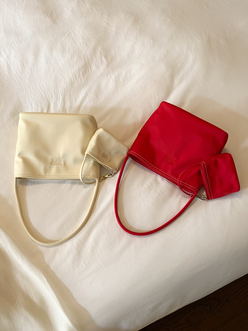 Two small shoulder bags with matching pouches in cream and red on a white bed