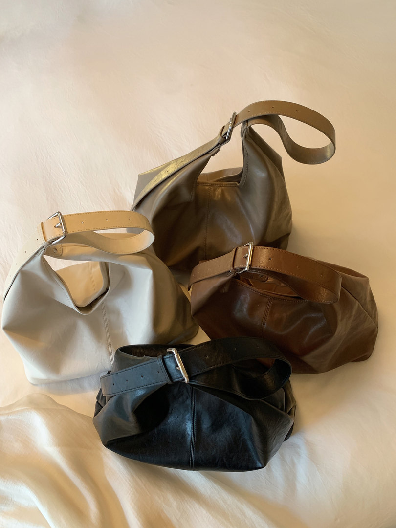 Four leather shoulder bags in assorted colors laid out on a light fabric background