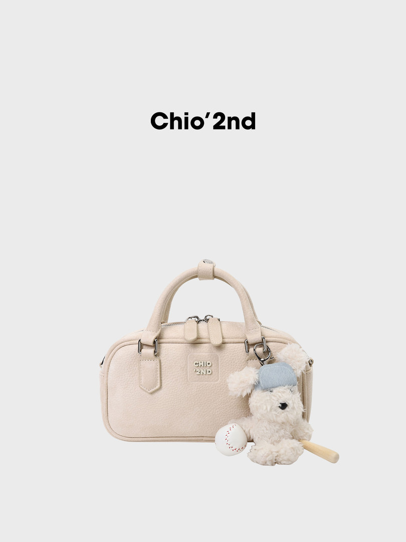 Beige structured handbag with a teddy bear charm on a white background