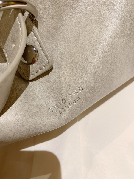 Close-up of a textured light-colored Chloé London handbag with metal hardware