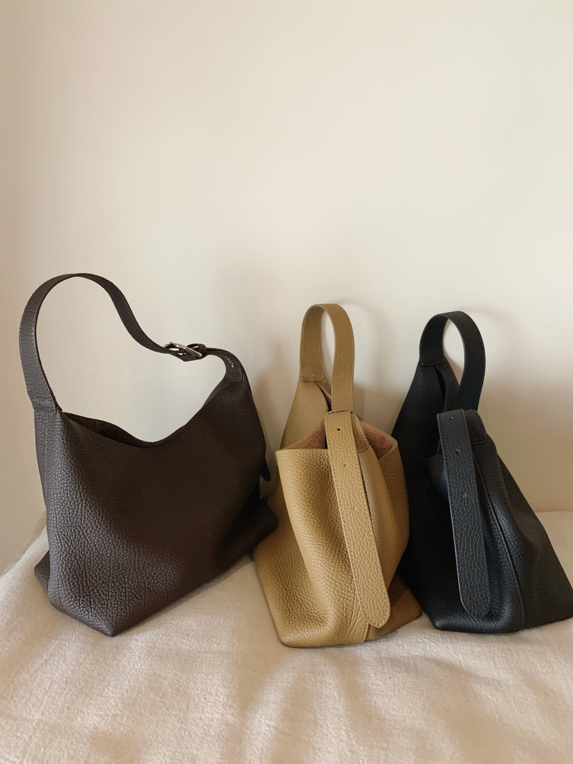 Three leather shoulder handbags in brown, tan, and black displayed on a fabric surface