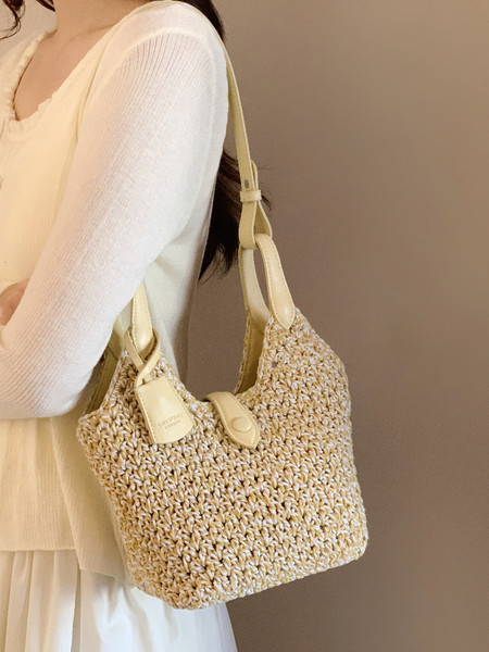 Woven beige shoulder handbag carried on a model