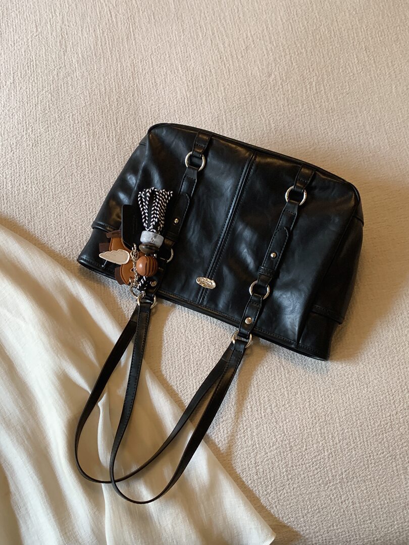 Black leather handbag with shoulder straps and charm accessory on a neutral background