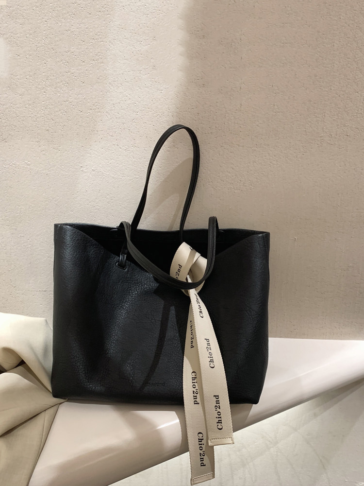 Black leather tote handbag with long straps and hanging logo ribbon