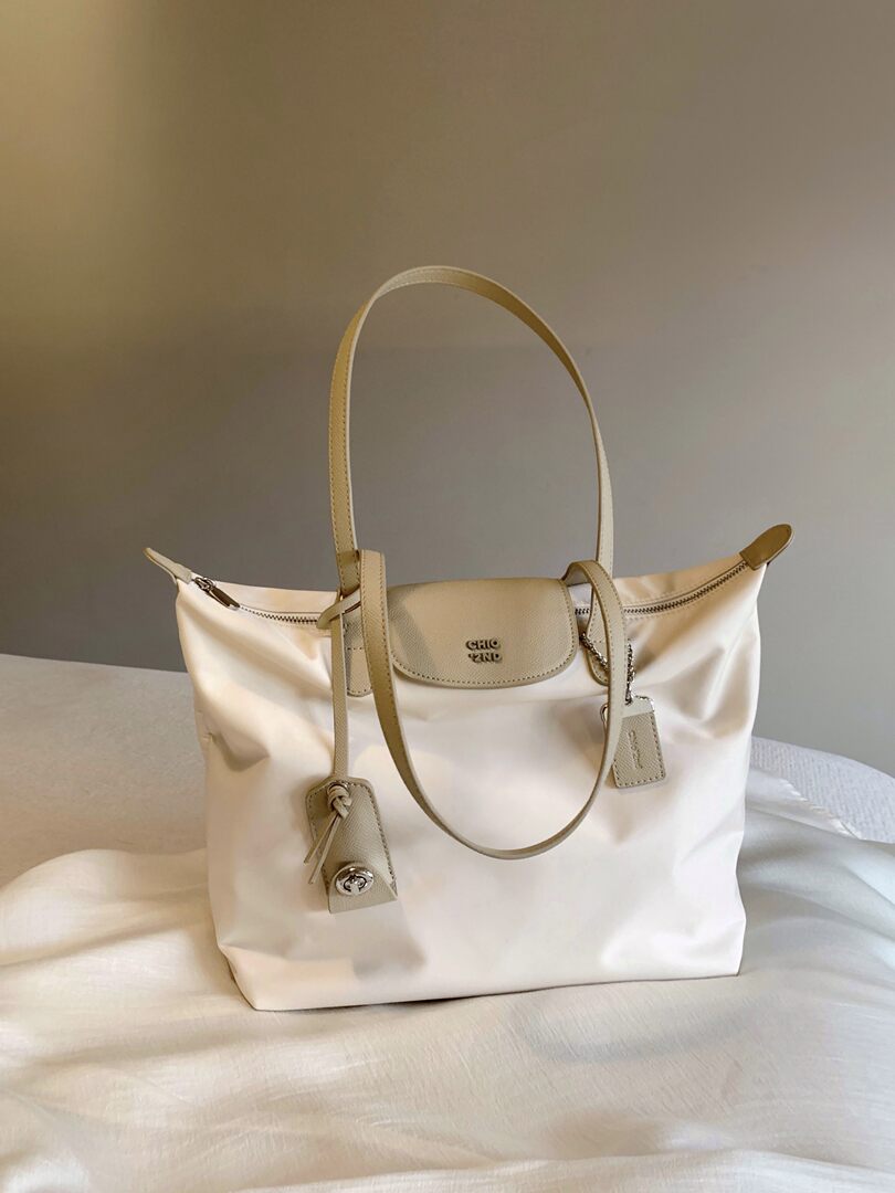 Cream and beige tote handbag with long straps displayed on a bed