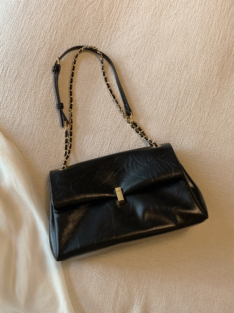 Black leather shoulder handbag with gold chain strap on a beige background