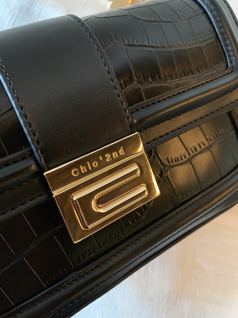 Close-up of a black crocodile-textured leather handbag with a gold clasp