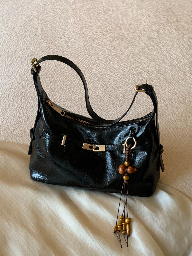 Black leather shoulder handbag with gold hardware and beaded charm on a bed