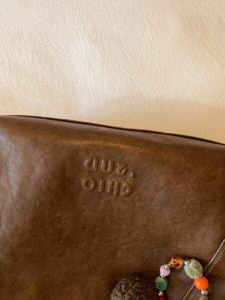 Brown leather handbag with embossed logo and beaded charm