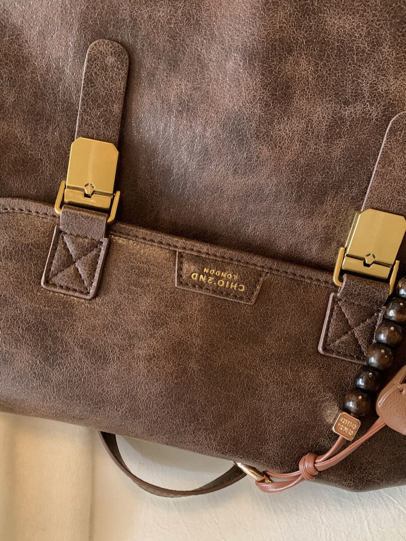 Brown leather handbag with gold buckle details and beaded charm