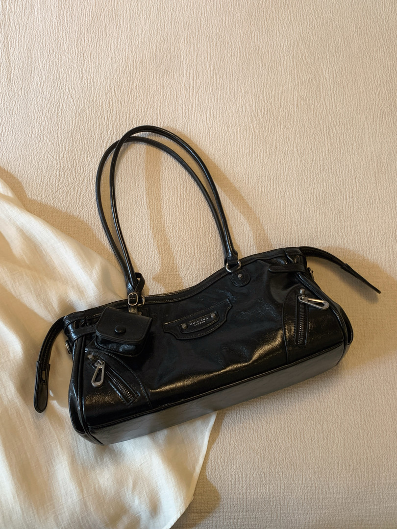 Black glossy handbag with long handles laid on a bed