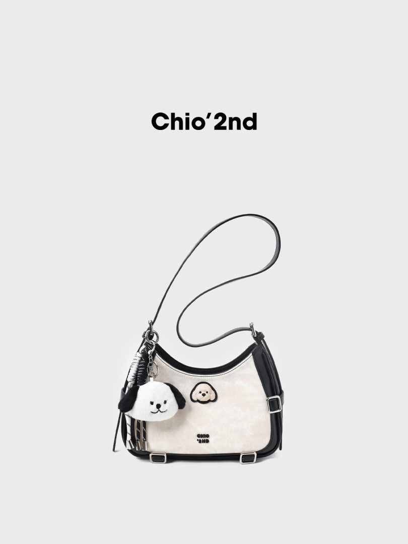 Black and white shoulder handbag with plush dog charms on a white background