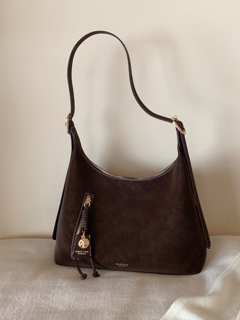 Dark brown shoulder handbag with gold hardware on a neutral background