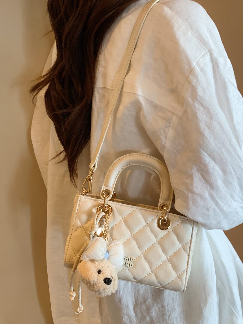 White quilted mini handbag worn on a shoulder strap with a teddy bear charm