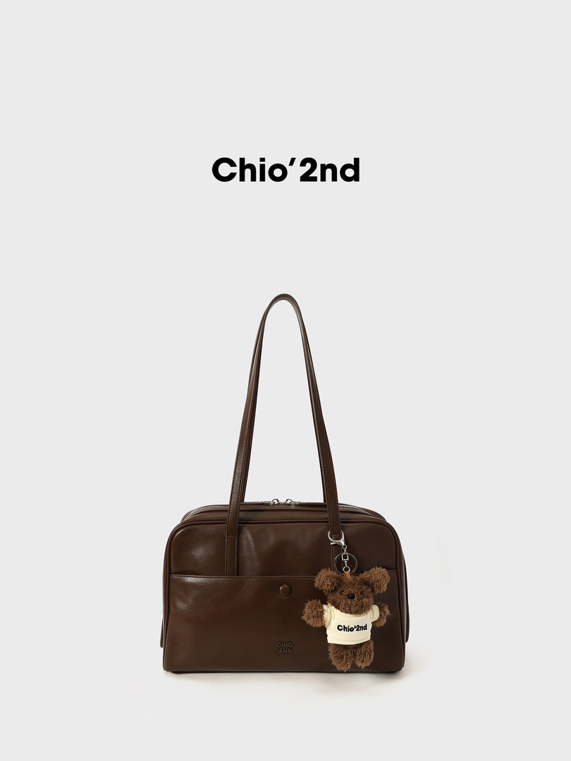 Brown leather shoulder bag with teddy bear charm on a white background
