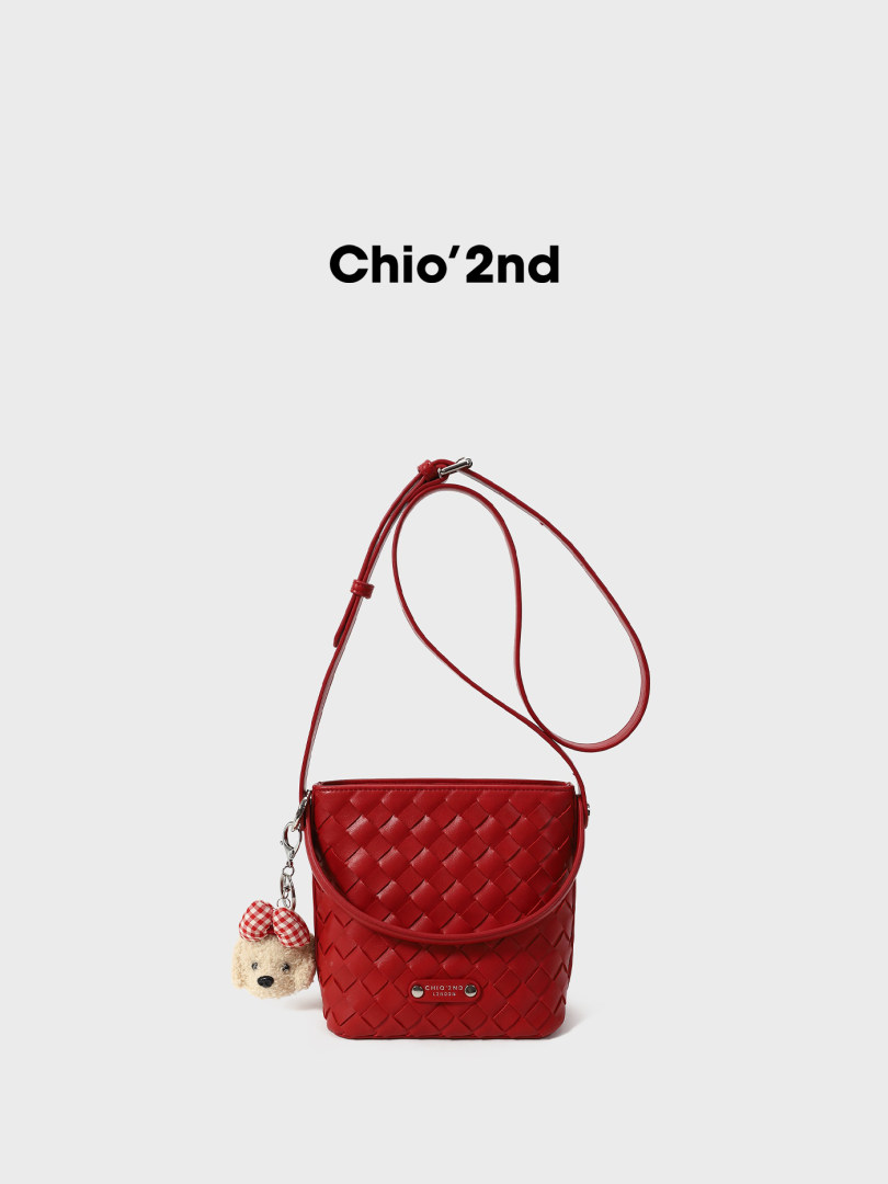 Red woven crossbody handbag with a teddy bear charm on a white background