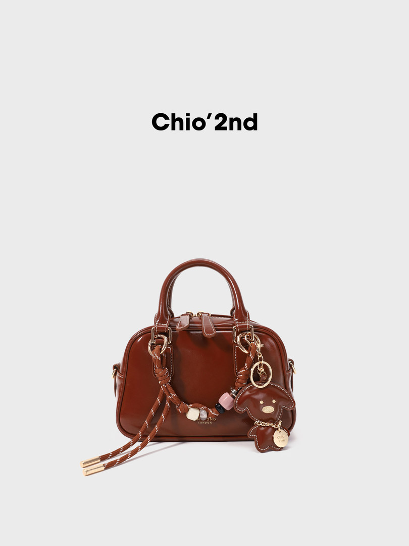 Brown leather handbag with charm accessories on a white background