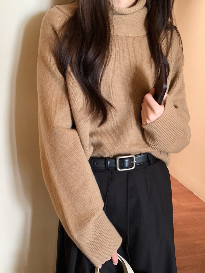 Woman wearing a beige turtleneck knit sweater with a black skirt and belt