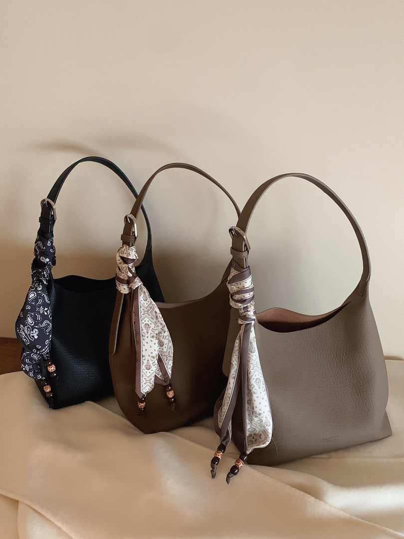 Three leather handbags with scarf handles displayed on a couch