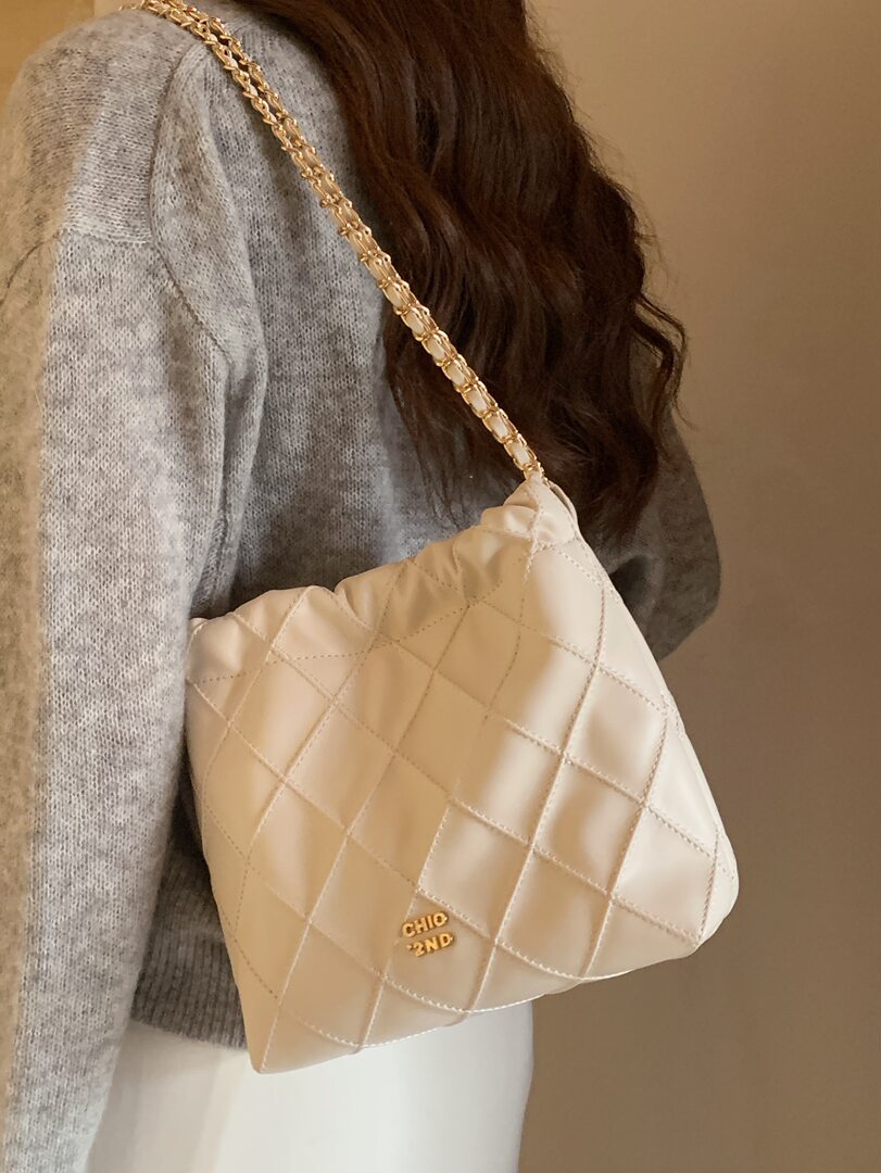 Cream quilted shoulder bag with gold chain strap worn by a model