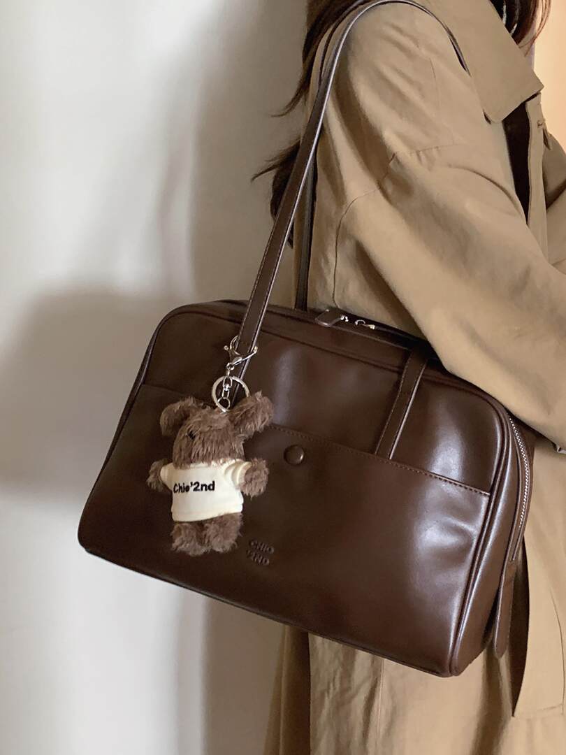 Brown leather shoulder bag with teddy bear charm being worn