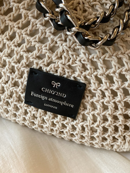 Close-up of a woven beige bag with a silver chain strap and brand tag