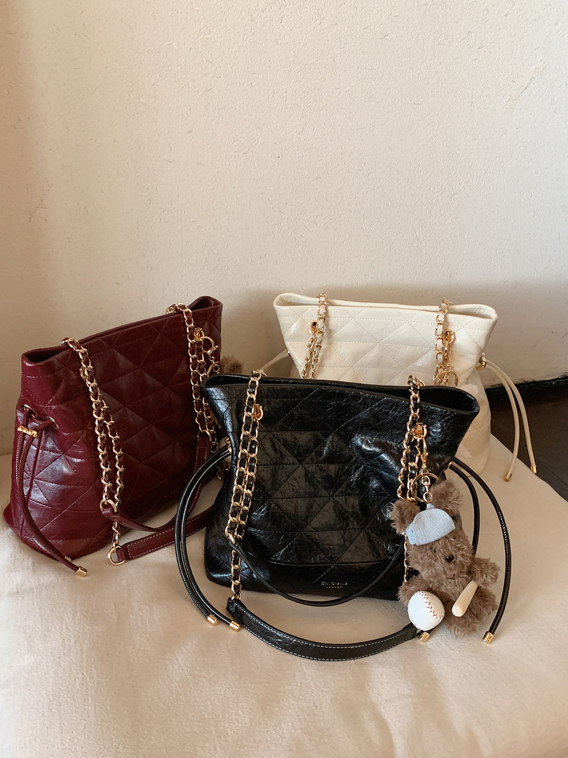 Three quilted chain-strap handbags in burgundy, black, and white on a neutral background