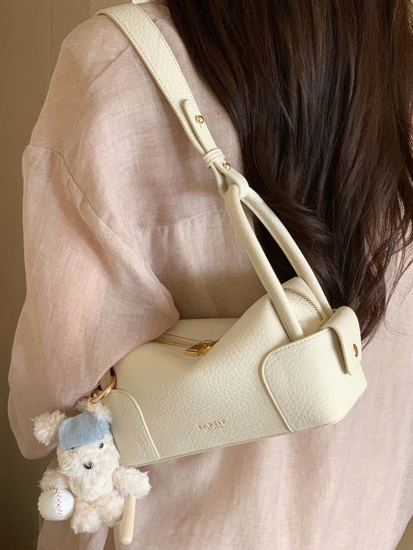 Cream textured shoulder handbag worn by a woman with a teddy charm
