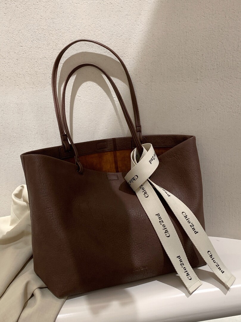 Brown leather tote bag with long handles and branded ribbon detail