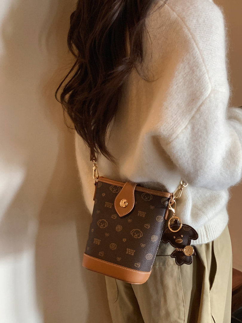 Brown monogram crossbody handbag worn by a model with a teddy bear charm