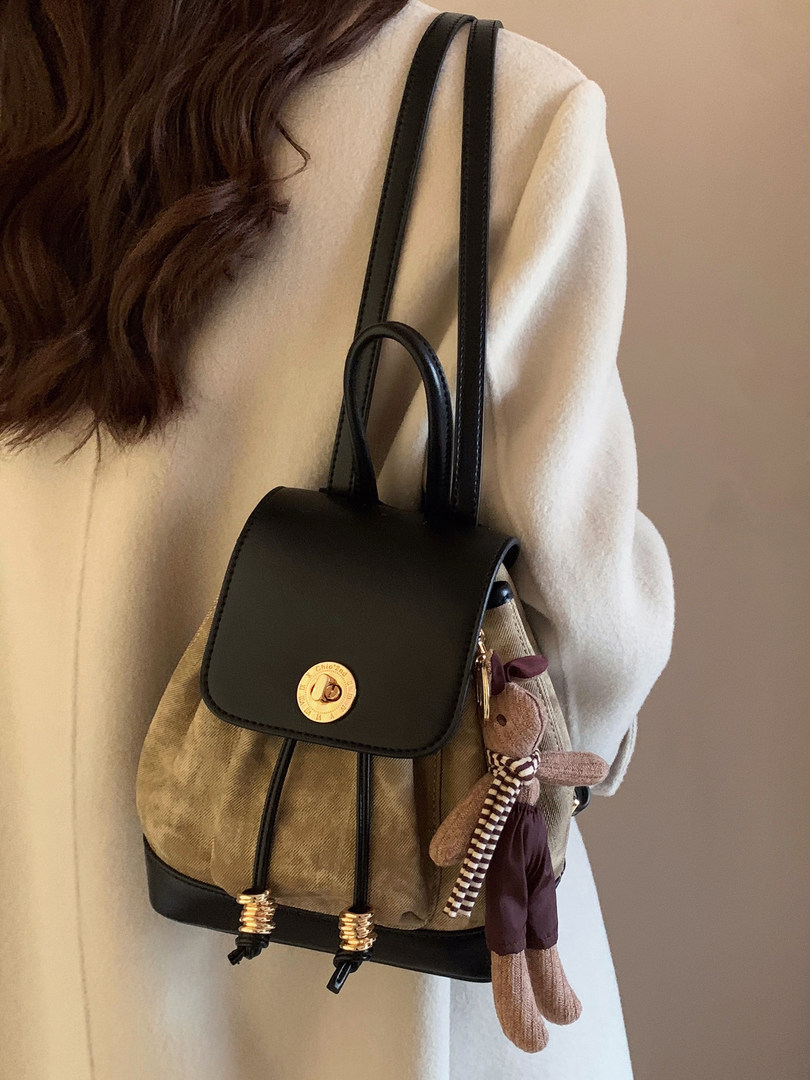 Black and beige backpack worn on a person with a small dangling charm