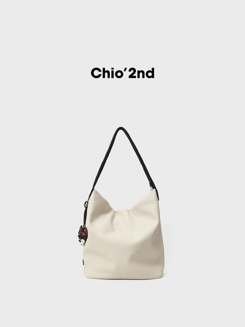 Cream shoulder tote bag with black braided strap on a plain background