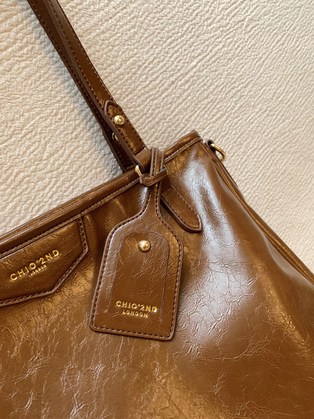 Brown leather handbag with gold-tone hardware and logo detail on a textured background