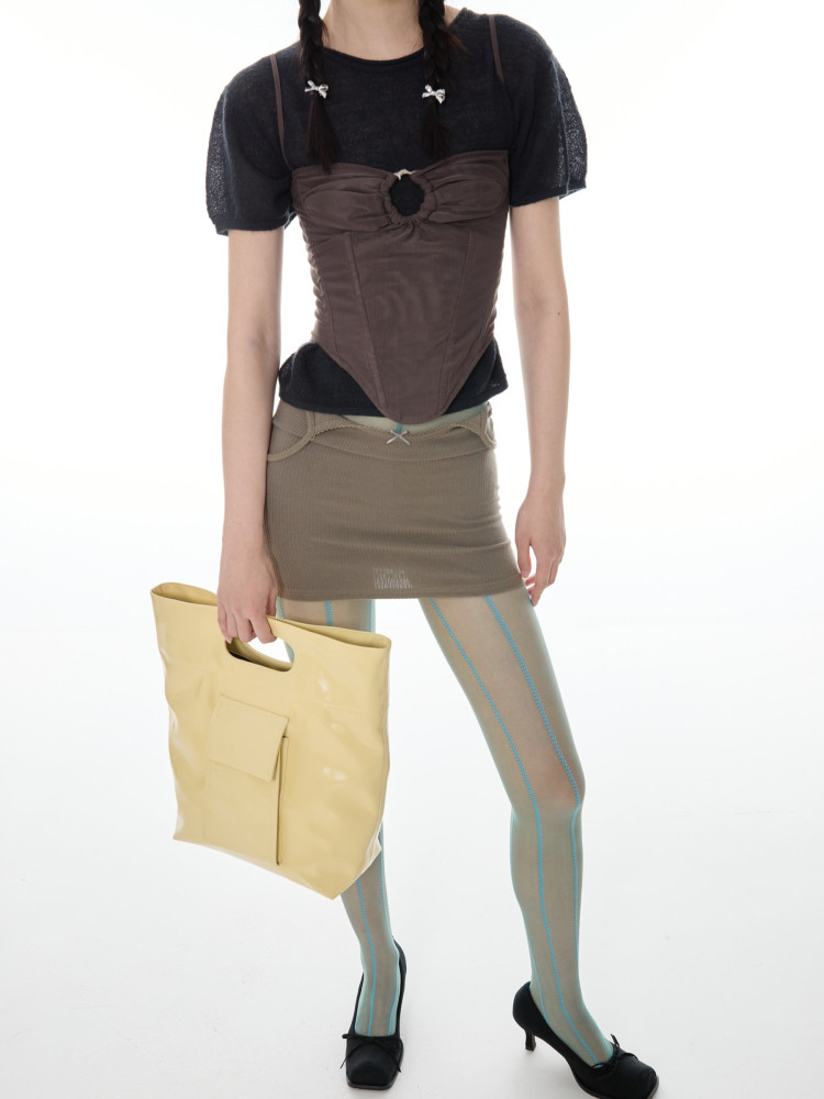 Model wearing a layered brown and black outfit with a yellow tote bag