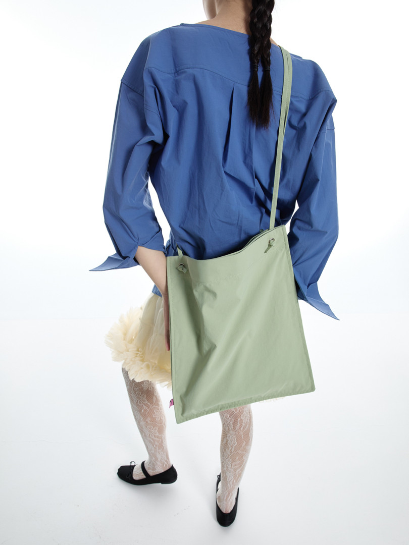 Model wearing a blue top with a light green shoulder bag
