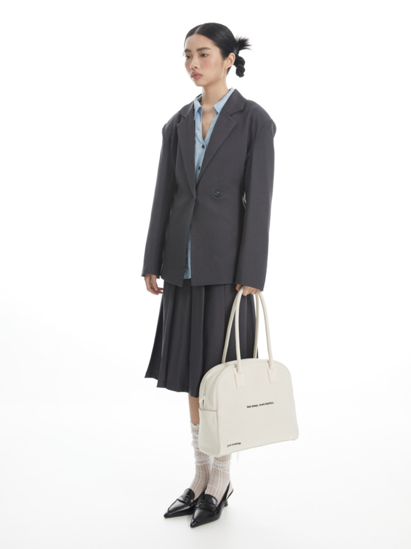 Woman wearing a dark blazer and skirt outfit while holding a cream tote bag