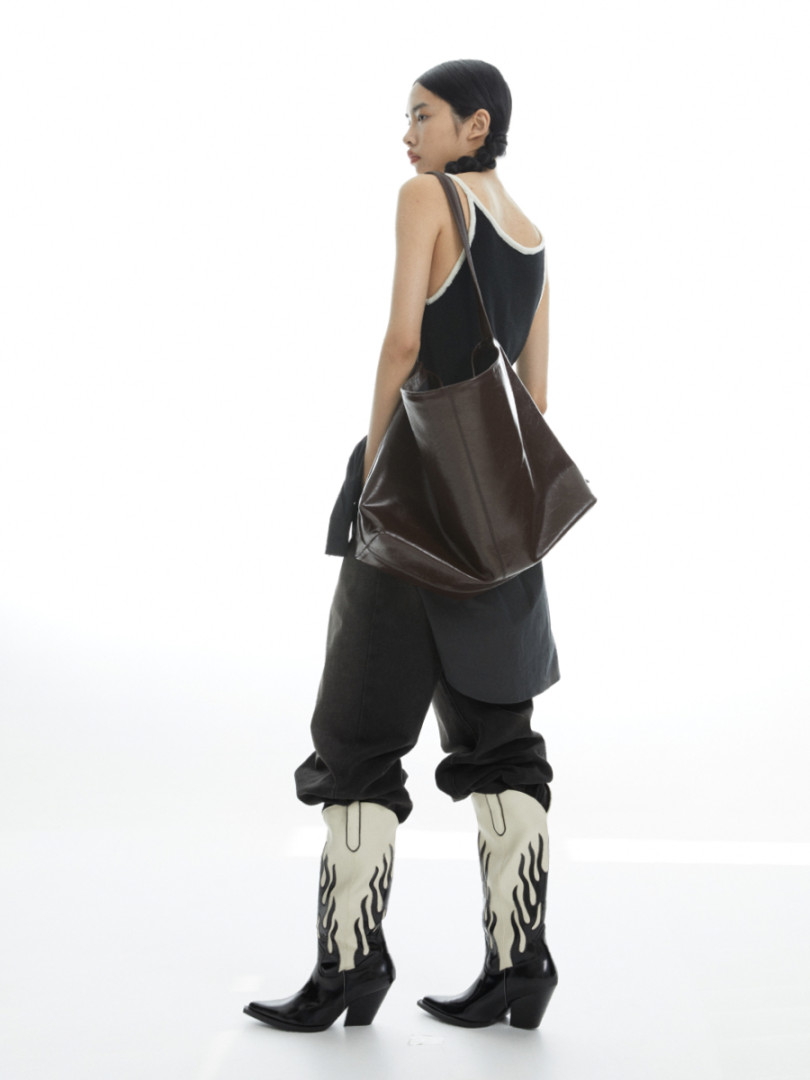 Model wearing a black outfit with cream flame-print cowboy boots and a large brown shoulder bag
