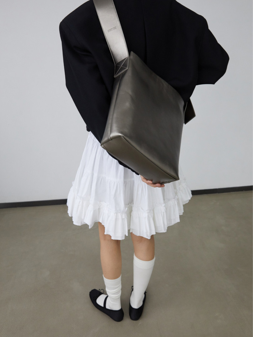 Model wearing a black top, white tiered skirt, and large shoulder tote bag