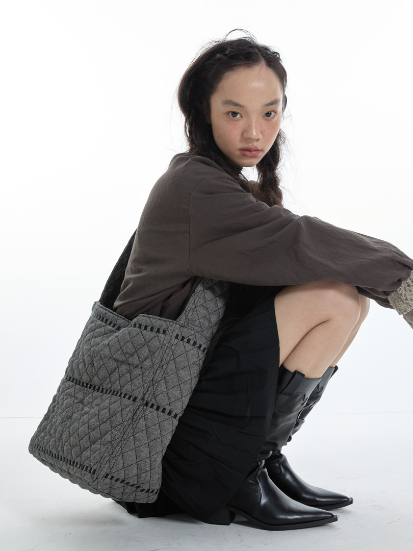 Model wearing dark outfit with black boots and a gray quilted tote bag