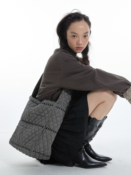 Model wearing dark outfit with black boots and a gray quilted tote bag